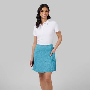 A woman wears a white polo shirt and a blue heathered skirt.