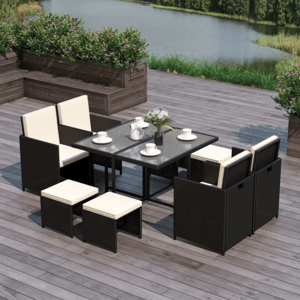 A modern outdoor dining set featuring a glass-top table, four cushioned chairs, and four small cushioned stools, all in a wicker design, situated on a wood deck overlooking a lake.