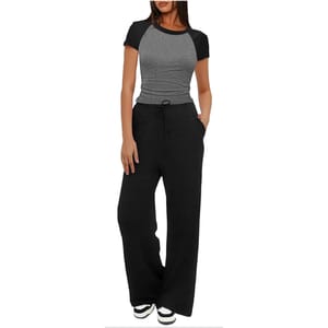 A person is wearing a two-tone fitted short-sleeve top with black sleeves and a gray body, paired with black wide-leg drawstring pants and black-and-white sneakers.