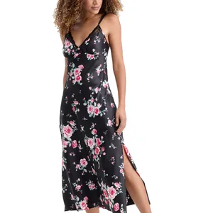 A woman wearing a black, floral-patterned slip dress with thin straps and lace detailing. The dress features pink and white flowers with a slit on the side.