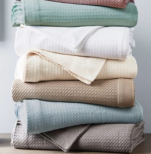 A stack of folded blankets in various colors including teal, white, beige, light blue, and gray.