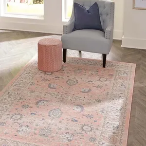 A gray wingback chair with a blue cushion, pink cylindrical ottoman, and a vintage-style pink area rug.