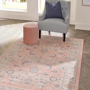 A gray wingback chair with a blue cushion, pink cylindrical ottoman, and a vintage-style pink area rug.