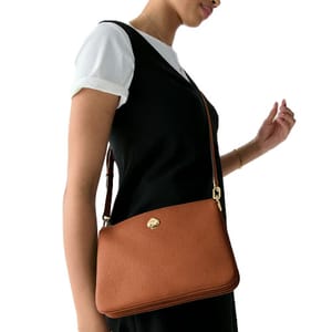 A person carries a brown leather handbag with a shoulder strap and gold hardware, worn over a white shirt and black dress.