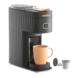 Single-serve coffee maker by Cuisinart, featuring a brew/cancel button, with an orange mug and coffee pods included.