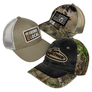 A 3-pack of baseball caps featuring different designs: one with a \“Drink Local\“ patch, another with a camouflage and black flag pattern, and the third with \“Team Realtree\“ on a black and green camo background.