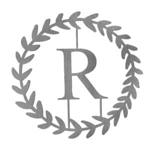 Monogram letter \“R\“ surrounded by a circular laurel wreath design, made of brushed metal.