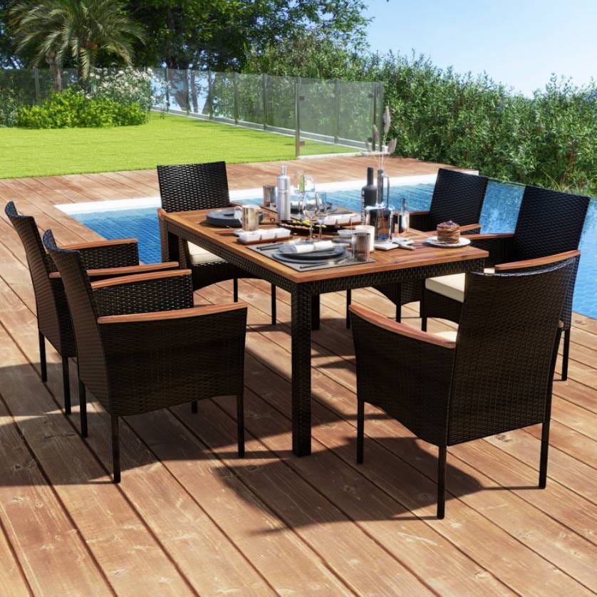 Outdoor wicker dining set featuring a rectangular table and six chairs, situated on a wooden deck beside a pool. The table is set with plates, glasses, and tableware.