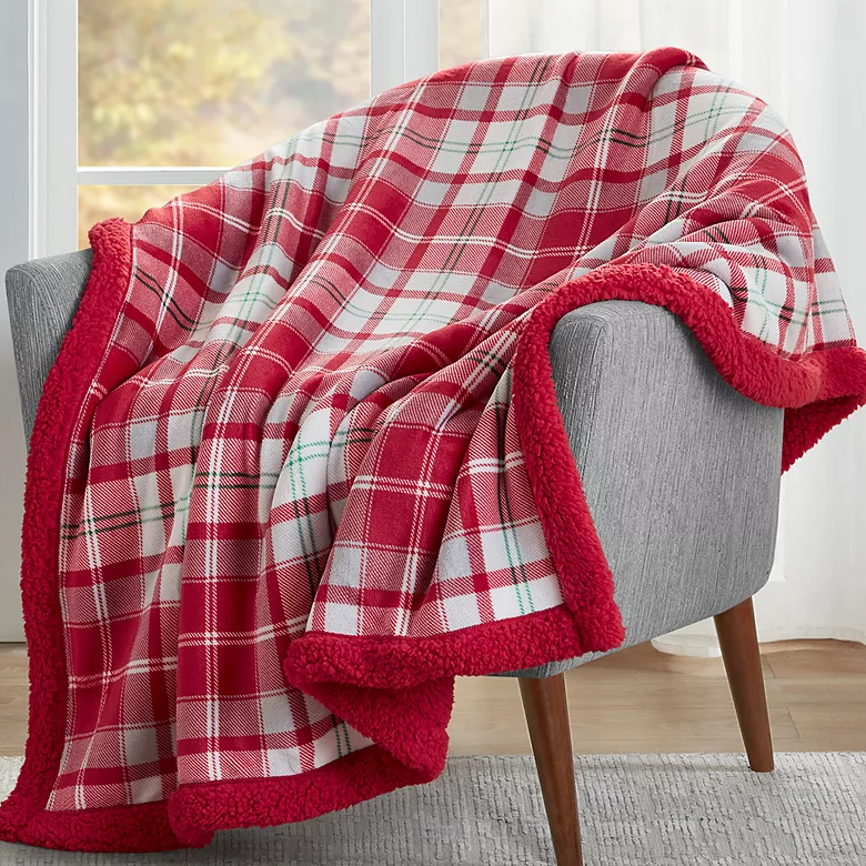 A red and white plaid throw blanket with a soft red sherpa trim is draped over a grey chair.