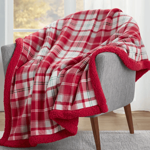 A red and white plaid throw blanket with a soft red sherpa trim is draped over a grey chair.