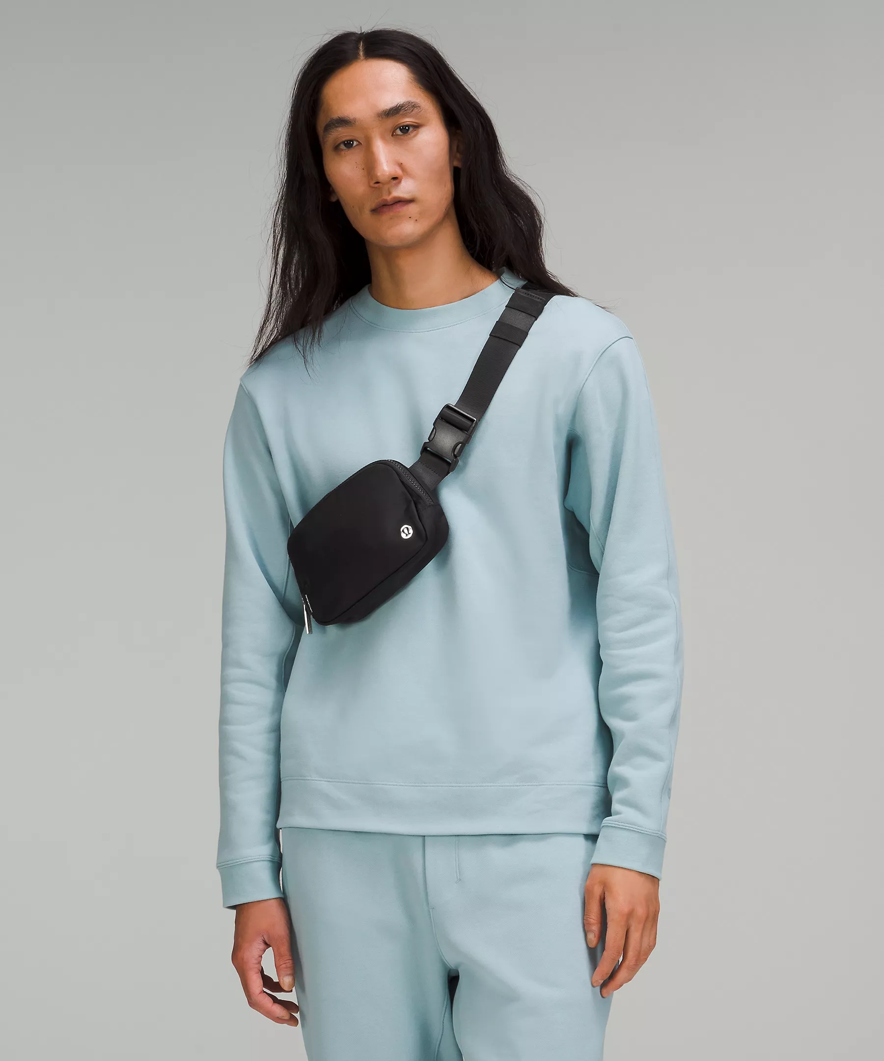 A person wearing a light blue sweatshirt and sweatpants set with a black crossbody bag.