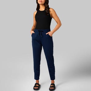 A woman is wearing a sleeveless black top and navy blue drawstring pants paired with black sandals.