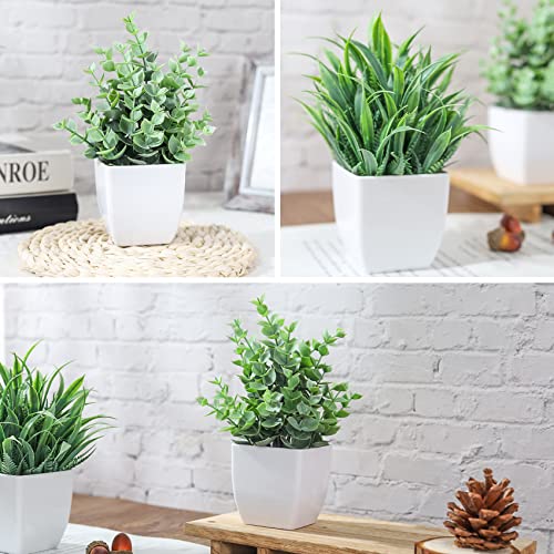 Two artificial plants in white square pots are arranged in different settings, one resembling eucalyptus and the other mimicking spiky green leaves.