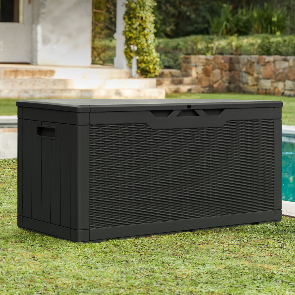 A black outdoor storage box with a wicker-style texture, situated near a pool in a garden setting.
