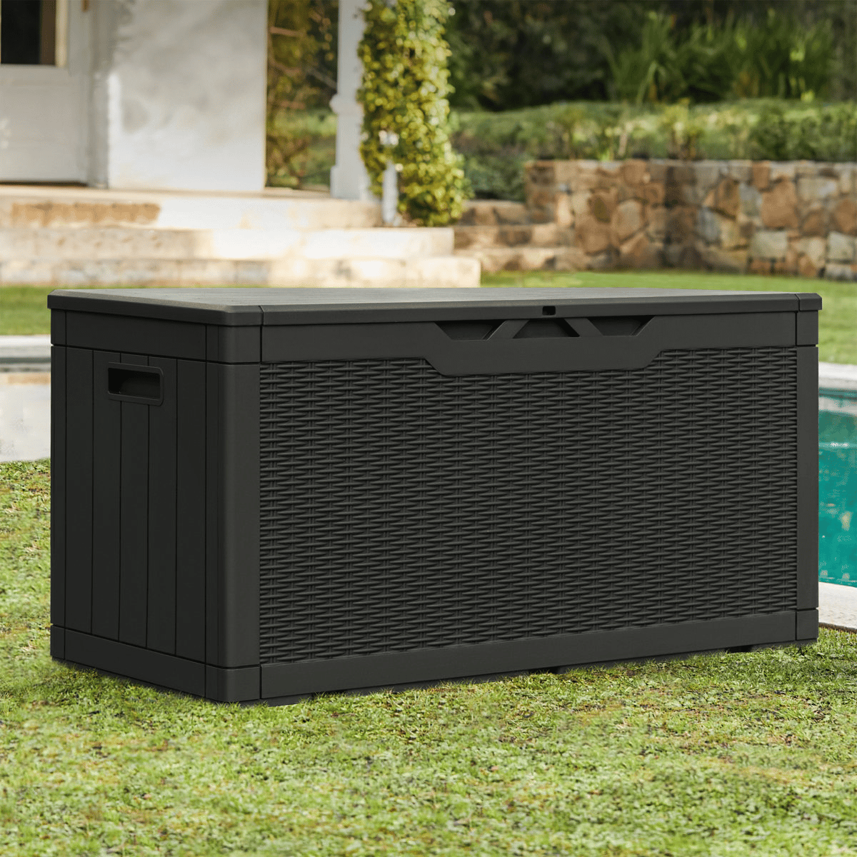 A black outdoor storage box with a wicker-style texture, situated near a pool in a garden setting.