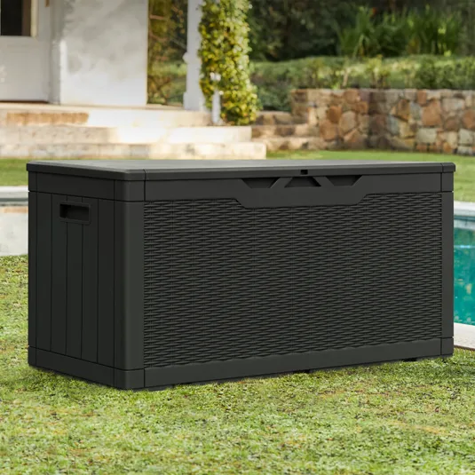 A black outdoor storage box with a wicker-style texture, situated near a pool in a garden setting.