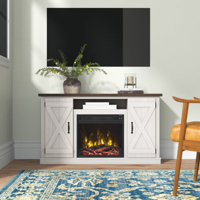 A white farmhouse-style TV stand with a dark top features barn-style doors, a central electric fireplace, and a TV mounted above.