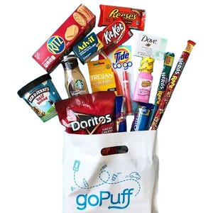 A goPuff bag contains Ritz crackers, Reese's, Kit Kat, Advil, a Dove bar, Trojan condoms, Tide To Go, Starbucks iced coffee, Ben & Jerry's ice cream, Doritos, Pepto-Bismol, a lighter, ChapStick, and Nerds Rope candy.