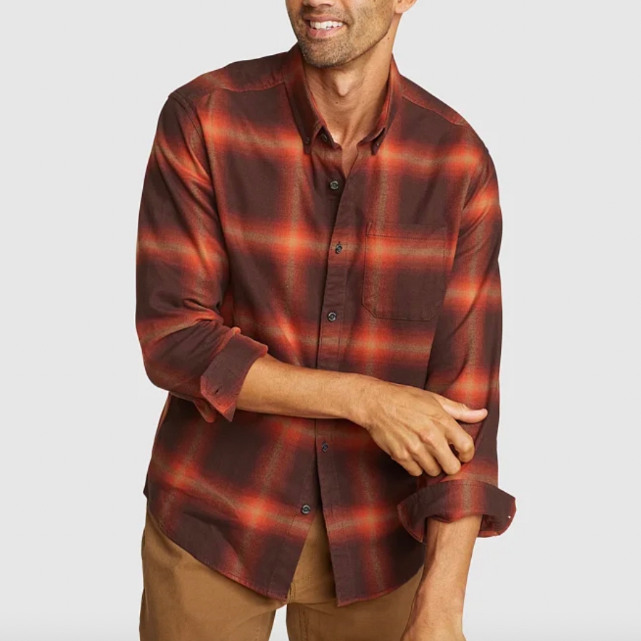 A man wearing a red and black plaid long-sleeve shirt with a front pocket, paired with light brown pants.