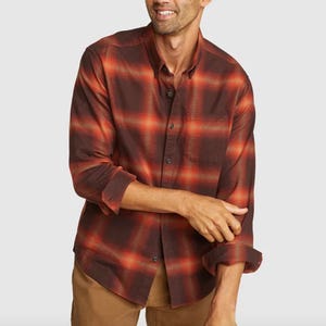 A man wearing a red and black plaid long-sleeve shirt with a front pocket, paired with light brown pants.