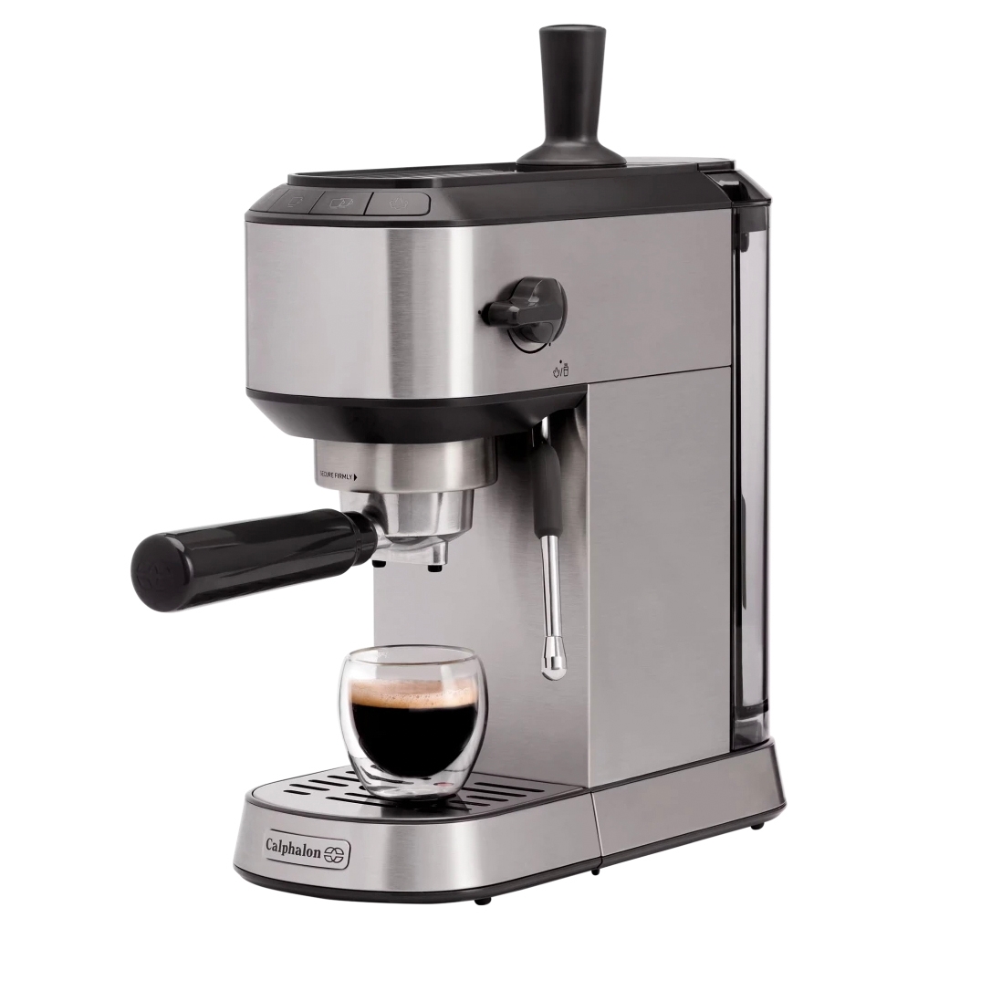 Calphalon Compact Espresso Machine with a sleek stainless steel finish, portafilter, and steam wand for frothing. A glass cup is placed under the spout, demonstrating its compact design.