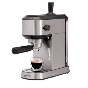 Calphalon Compact Espresso Machine with a sleek stainless steel finish, portafilter, and steam wand for frothing. A glass cup is placed under the spout, demonstrating its compact design.