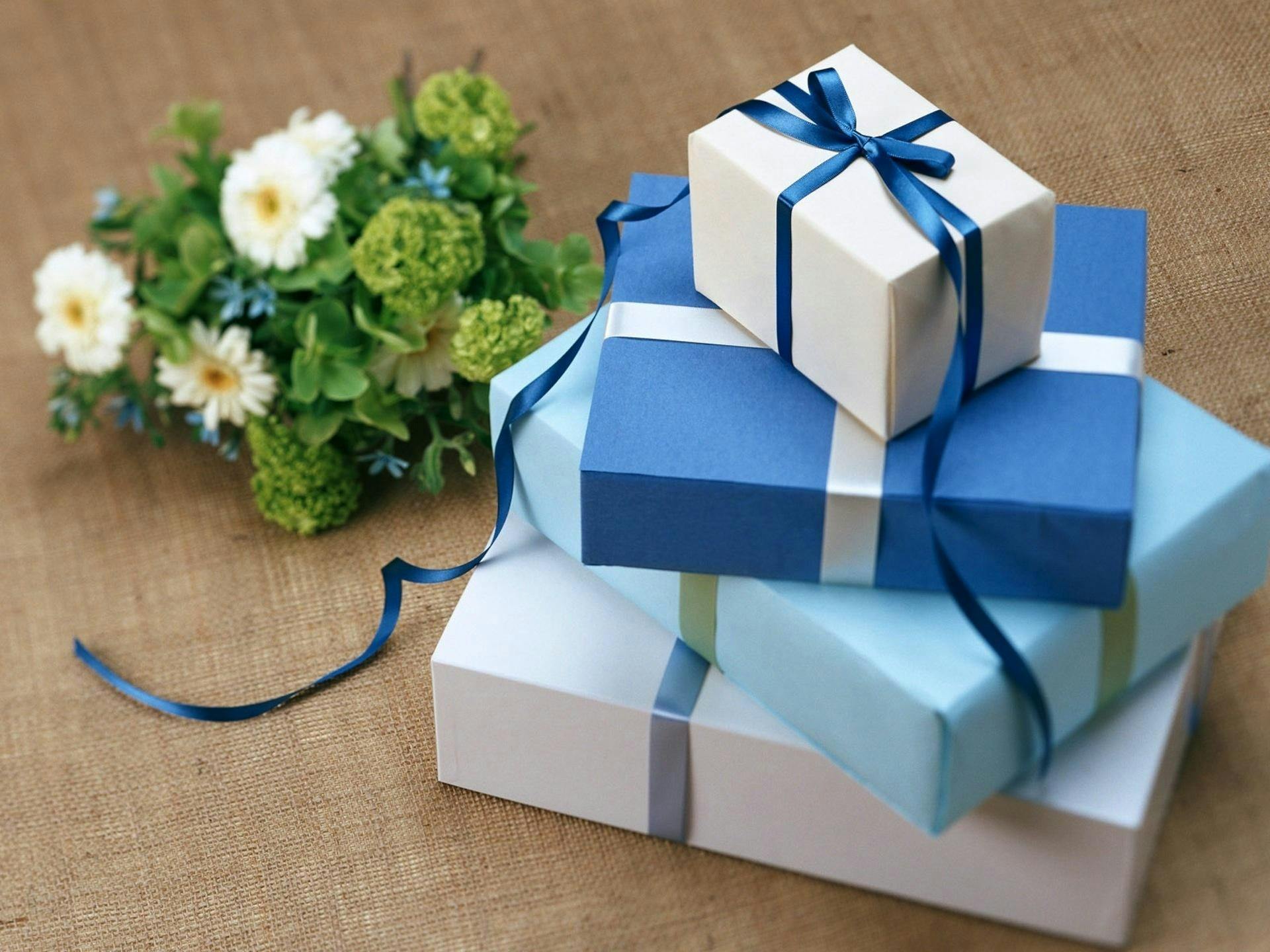 A bouquet of flowers next to stacked gift boxes with blue and white wrapping and ribbons.