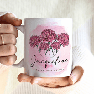 A personalized white mug featuring a pink watercolor background with illustrations of pink flowers and the name \“Jacqueline\“ written in cursive, accompanied by the phrase \“Super Mom, Always.\“