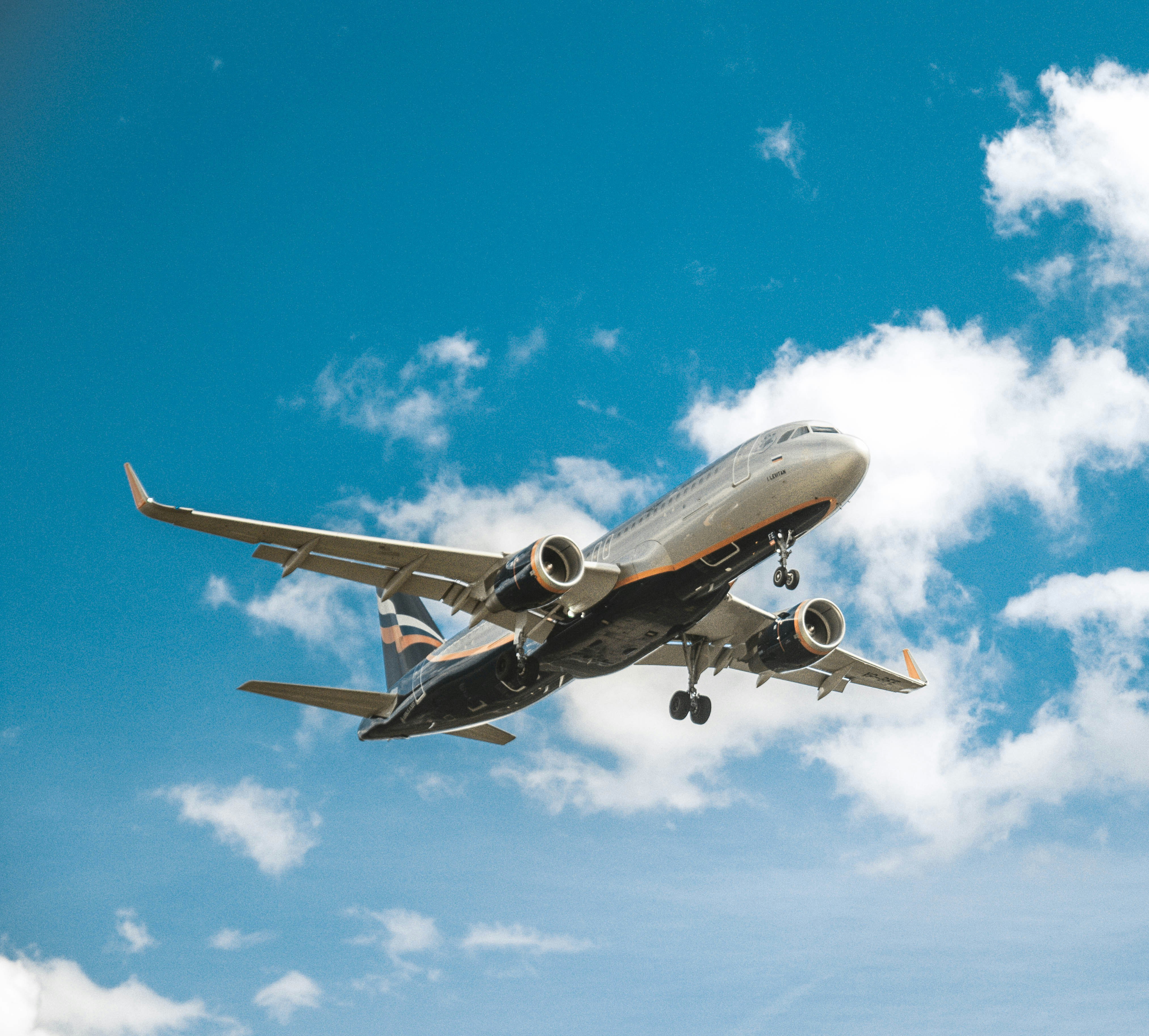 A commercial airplane is shown mid-flight against a blue sky with scattered clouds.