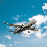 A commercial airplane is shown mid-flight against a blue sky with scattered clouds.