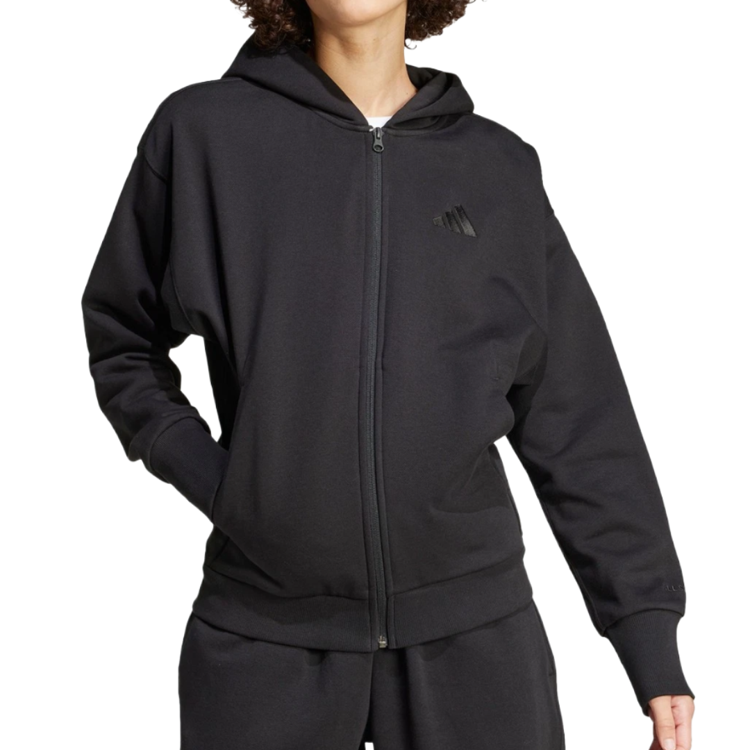 A person is wearing a black zip-up hoodie with a hood and elastic cuffs, featuring a subtle logo on the chest. They are also wearing matching black sweatpants.