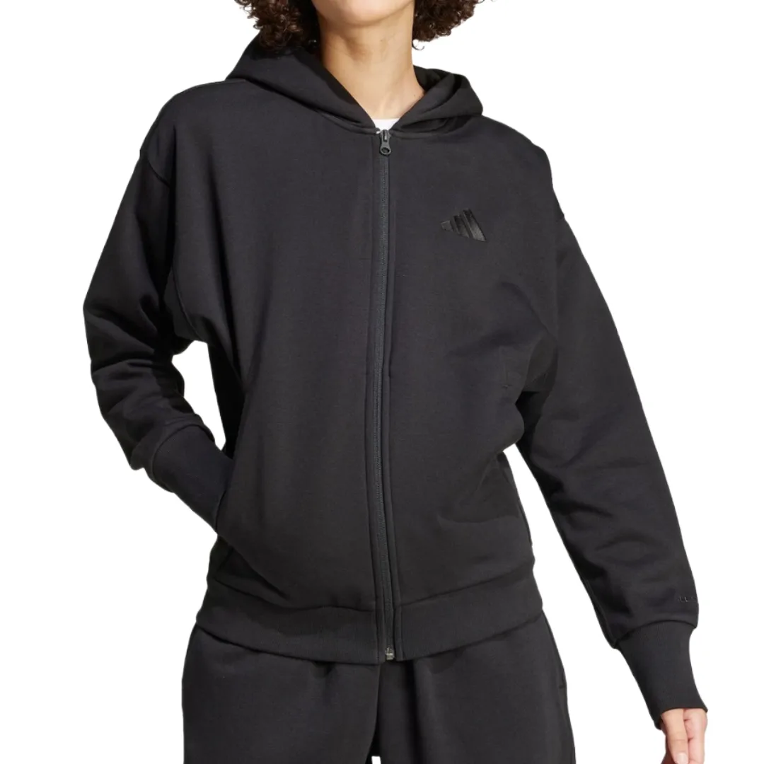 A person is wearing a black zip-up hoodie with a hood and elastic cuffs, featuring a subtle logo on the chest. They are also wearing matching black sweatpants.