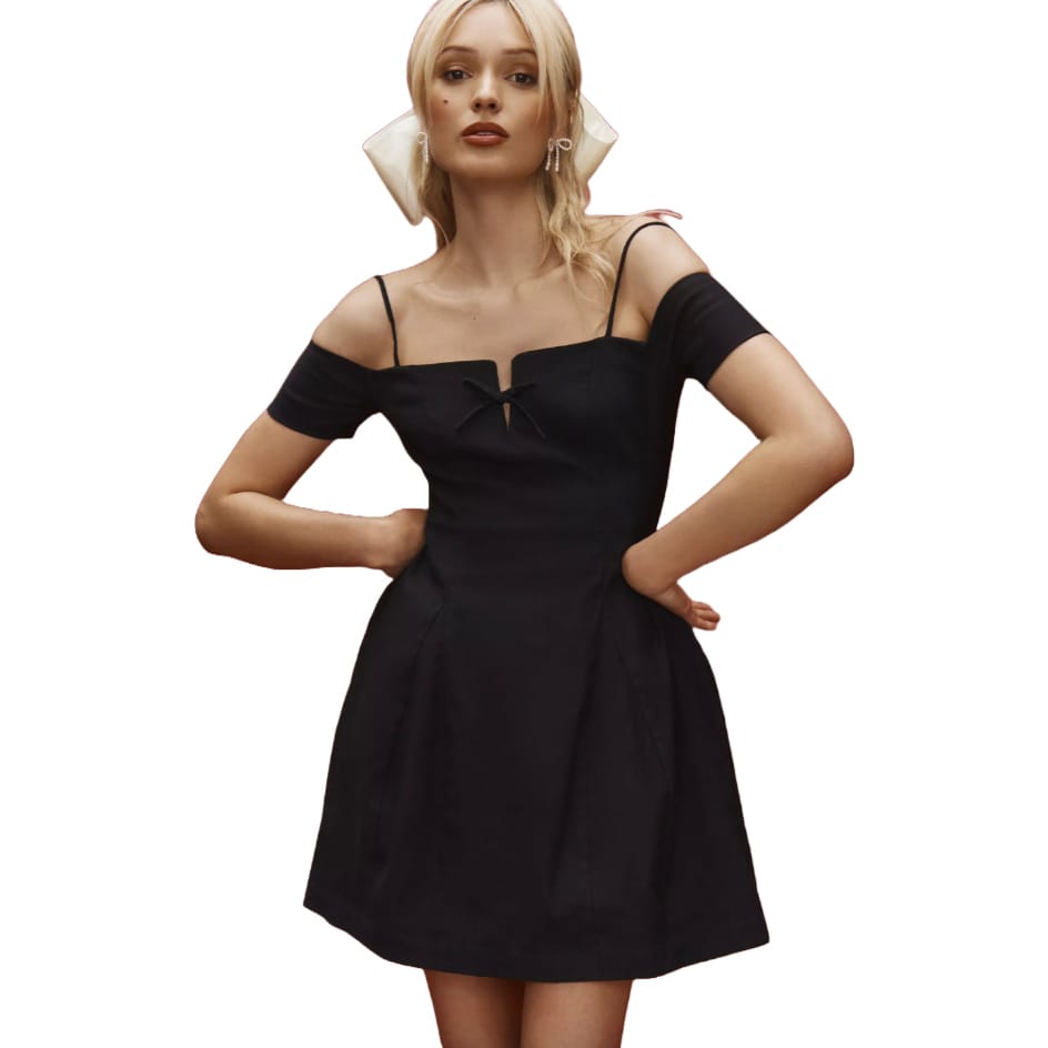 A black off-the-shoulder mini dress with thin spaghetti straps, featuring a slight cutout and bow detail at the neckline. The dress has a fitted bodice and a flared skirt.