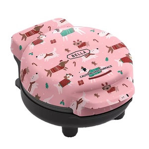 A pink Bella Holiday Mini Waffle Maker featuring a festive design with dogs in holiday sweaters, reindeer antlers, and surrounded by gifts and candy canes.