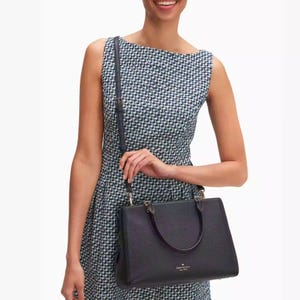 A woman wearing a houndstooth dress and carrying a textured black leather shoulder bag with a brand logo.