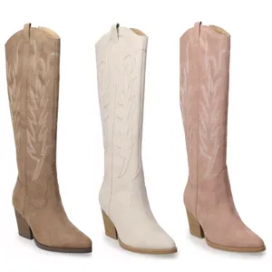 Three suede cowboy boots in brown, white, and pink, featuring embroidered designs and mid-height block heels.