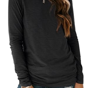 A person wearing a long-sleeved, dark-colored top paired with distressed jeans. The outfit includes simple jewelry like a necklace and bracelet.