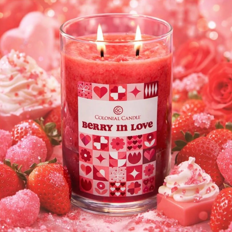 A lit Colonial Candle features the scent \“Berry in Love,\“ surrounded by strawberries, pink sugar decorations, and a pink frosted cupcake.