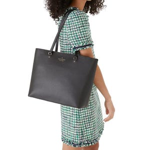 A person is carrying a black leather tote bag and wearing a short-sleeved green and white tweed dress.