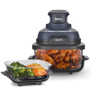 A Ninja food processor labeled \“CRISPi\“ is shown with prepared dishes, including buffalo wings and broccoli with salmon, in transparent containers.