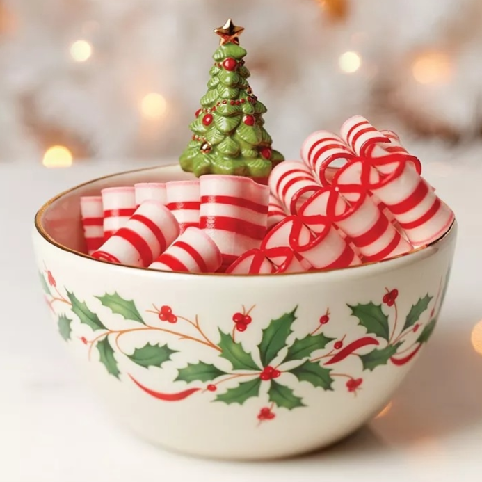 A decorative bowl with holly patterns, filled with peppermint candies in red and white stripes. A small ceramic Christmas tree decorates the center.