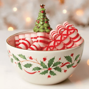 A decorative bowl with holly patterns, filled with peppermint candies in red and white stripes. A small ceramic Christmas tree decorates the center.