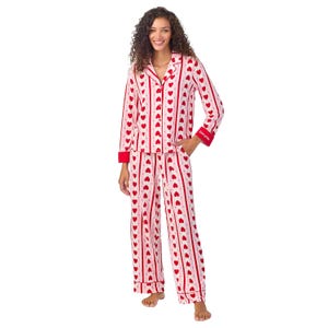 A woman is wearing a pajama set with red hearts and stripes on a white background. The set includes a long-sleeve top with red cuffs and matching wide-leg pants.