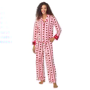 A woman is wearing a pajama set with red hearts and stripes on a white background. The set includes a long-sleeve top with red cuffs and matching wide-leg pants.