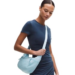 A person wearing a dark blue dress is carrying a light blue shoulder bag with multiple zipper compartments.