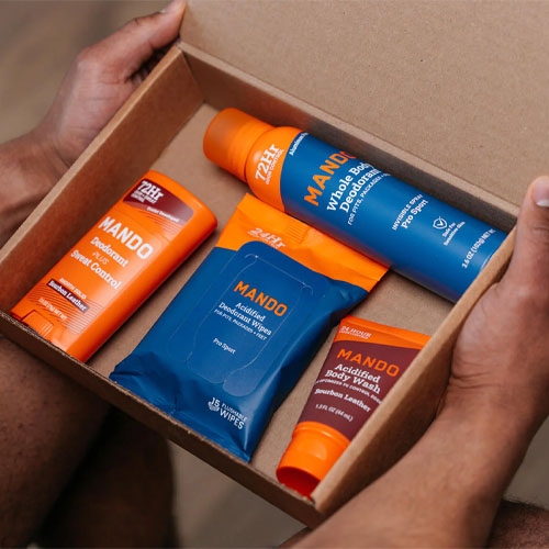 A box contains Mando products: accelerator control, face lotion, body moisturizer, and body wash, along with wet wipes, all in orange and blue packaging.