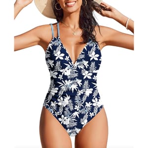 A one-piece swimsuit with a deep V-neck and blue-and-white floral print, featuring adjustable straps. The wearer accessorizes with a straw hat, hoop earrings, a necklace, and a bracelet.