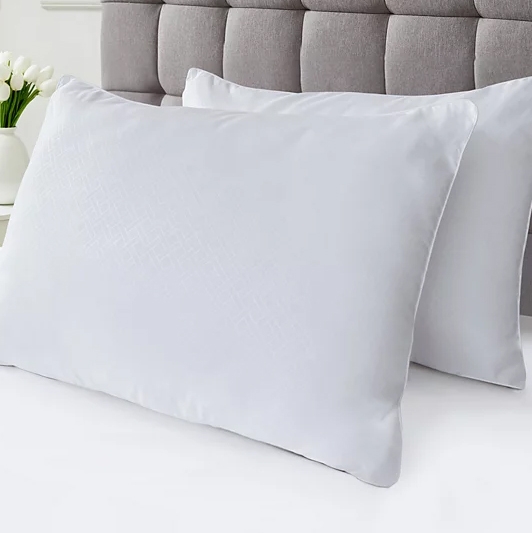 Two white pillows are placed on a bed with a tufted gray headboard in the background.