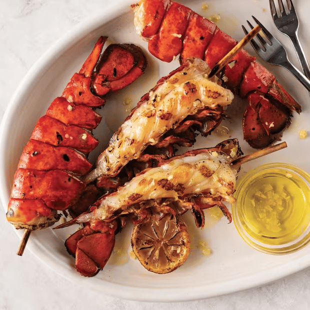 Grilled lobster tails with garlic butter and lemon slices, served with a side of melted butter.