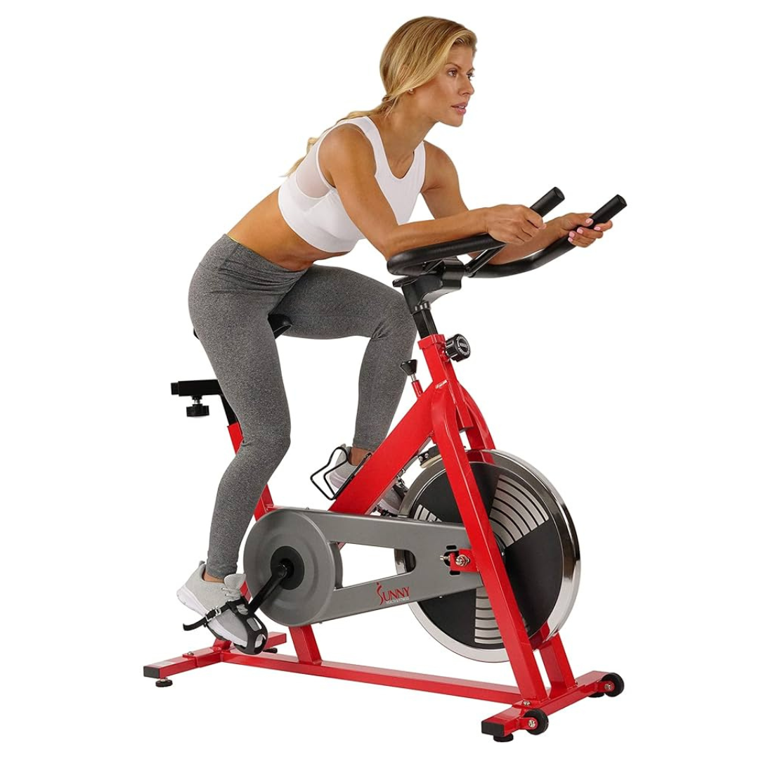 A woman exercises on a red stationary bike from Sunny Health & Fitness, wearing a white sports bra and gray leggings.